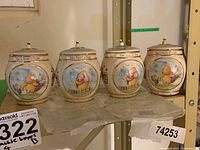 Front view showing four Winnie the Pooh honey pot music boxes lined up in a row showing different Pooh and Piglet scenes and text on tops.