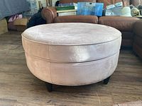 Front angled view of the pink ultrasuede ottoman showing details of the fabric, stitching, and supporting legs.