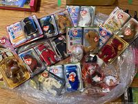 Overview photo showing a collection of multiple Ty Beanie Babies plush toys in plastic packaging, laid out on a wooden surface.