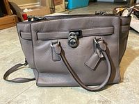 Front view of taupe leather Michael Kors purse with handles and shoulder strap visible
