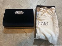 Black velvet Badgley Mischka clutch with crystal brooch detail, dust bag, and box visible