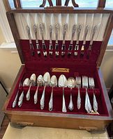 Full open view of the wooden case with silver plated cutlery arranged inside showing completer assortment of forks and spoons.