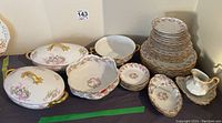 Full view of the china lot showing covered dishes, bowls, plates and smaller dishes stacked together on a table.
