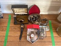 Overview of assorted watches and costume jewelry on wooden floor including watches in boxes, metal bracelets and rhinestone accessories.