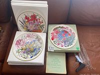 Four Wedgwood Plates in white foam packaging and one plate in green foam on couch with clear acrylic stands and booklet