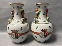 Front view of both vases showing floral painted decorations, religious crests with crowns, and applied 3D floral accents on necks.