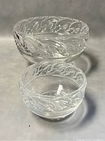 Two clear Tiffany & Co. crystal bowls with dolphin design on rim, one larger and one smaller, placed side by side on a grey cloth background.