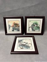 Three framed Japanese prints laid flat showing scenic waterviews with bridges and houses.