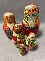 Five Russian nesting dolls arranged by size showing characters including Santa Claus, girl, bear, snowman, and small girl.