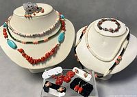 Collection of assorted necklaces and earrings displayed on two white bust stands and black card holders
