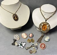 Full lot shows 21 inch GERRYS necklace with large cameo pendant on stand, additional cameo brooches and pins arranged in front