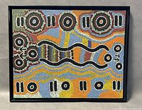 Full view of the framed native dot painting showing vibrant concentric circle patterns and wavy lines in black, white, orange, blue, yellow, and brown colors.