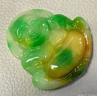 Close-up of a natural jade Buddha pendant showing green and brown color hues and carved details.