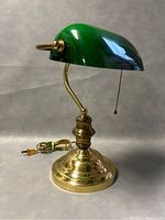 Front angled view of the brass bankers lamp with green glass shade and pull chain.