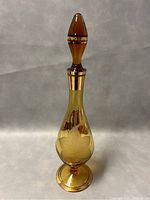 Full view of the amber glass genie bottle decanter with stopper, showing the shape and gold detailing.