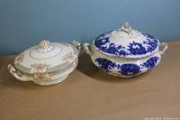 Two soup tureens side by side, showing top and handles, against a blue background