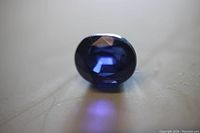 Close-up photo of the oval cut blue sapphire loose gemstone showing facets and deep blue color on a light surface.