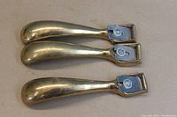 Top view of three brass spoon planes aligned, showing the polished brass handles and metal cutters held with screw fasteners.