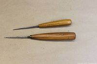 Two small carving gouges with wooden handles lying on a neutral surface.