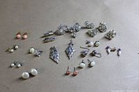 Top view showing 14 pairs and 2 single costume jewelry earrings including pierced and clip-on styles in various colors and materials such as faux pearls, rhinestones, and metal