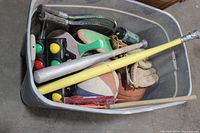 Plastic crate with assorted kids sports equipment including baseball gloves, basketballs, balls, skateboard, wiffle ball bat, and bocce balls