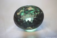 Close-up photo of the large green tourmaline oval cut gemstone showing the top facets and rich green color.