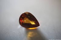 Pear-shaped orange garnet loose gemstone shown from top-down angle, highlighting facets and color.