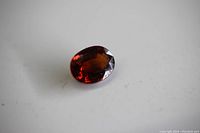 Close-up photo of oval faceted garnet loose gemstone on a white background showing its deep red color and facets.