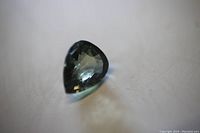 Close-up photo of the pear cut green Tourmaline loose gemstone showing its facets and green hue on a light surface.