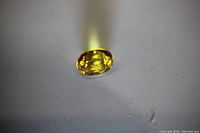 Oval cut yellow sapphire gemstone displayed under light showing bright yellow color and internal facets.