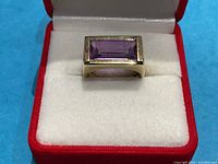 Front view of ring showing rectangular emerald-cut purple amethyst in bezel setting inside red jewelry box