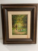 Framed oil painting of hunter with dog in forest pathway with bright light background.