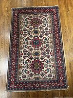 Full view of the cream background Persian rug with intricate red, blue, and other colorful motifs lying flat on a wooden floor.