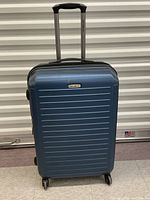 Front view of the blue Samsonite suitcase showing horizontal ridges and four spinning wheels.