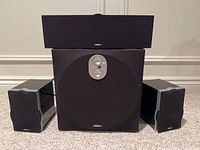 Front view showing four side speakers, one subwoofer with mesh grille, and one center speaker stacked on top