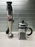 Both immersion blender and French press displayed together on countertop showing full height and detail.