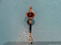 Front view of watch with black dial and silver-tone bangle bracelet on blue background