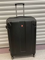 Front view of a large hard shell black suitcase with Swiss Gear logo in the center and four spinning wheels visible.