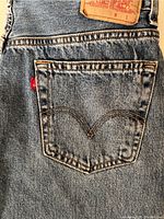 Close-up of back pocket showing Levi's arcuate stitch design and red tab, with partial view of leather patch on waistband.
