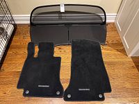 Photo showing two black car mats and a pull-down screen protector laid on wooden floor.