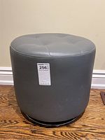 Front perspective showing full height and tufted top of round grey leather stool with some surface scuffs and chrome base visible