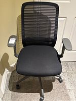 Front view of black office chair showing mesh back, cushioned seat, and armrests.