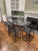 Six wrought iron chairs arranged around oval tempered glass tabletop on table frame
