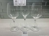 Three clear wine glasses (Riedel, Birks) with differing bowl shapes on countertop with backsplash tiles.