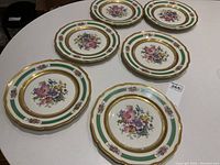 Full view of the 6 decorative plates displayed on a table showing the floral pattern and green and gold accents.
