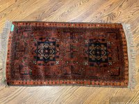 Top-down photo of small Persian carpet mat showing full design and fringes on wooden floor.