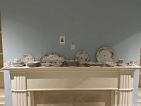Wide view of the entire set of vintage Limoges china displayed on a white mantle, showing cups, saucers, plates, platters, and small bowls with a floral design and gold trim.