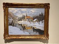 Framed winter landscape painting hanging on a wall showing the entire piece and ornate gold frame