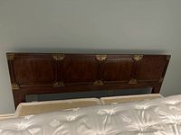 Front view of king size headboard showing four large decorative wood panels with brass corner brackets on each panel