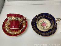 Two vintage Ansley cup and saucer sets side by side, navy blue with pink rose and burgundy with gold patterns